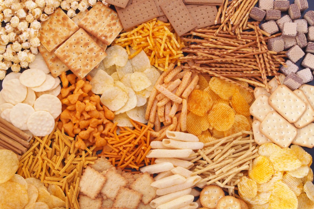 Assorted snacks including crackers, crisps and pretzels arranged on a dark surface